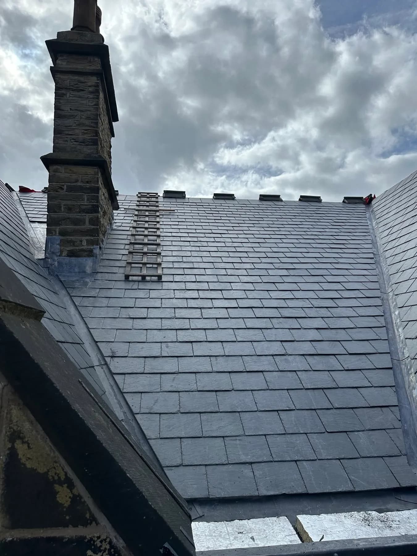 A slate roof and a tall brick chimney stack under a cloudy sky
